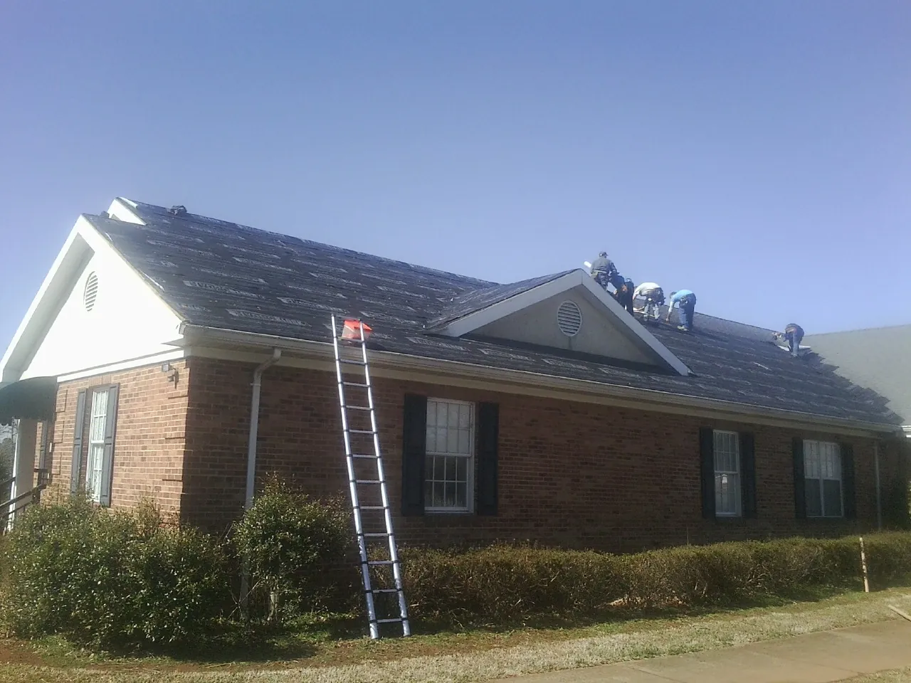 Crew tearing shingles off a brick ranch roof with a ladder set — Metal Roof Repair work by our crew in Callao