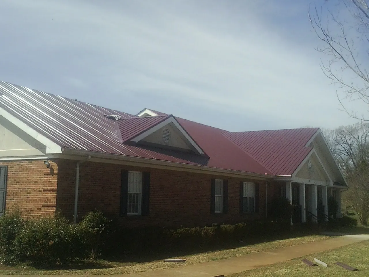 Red metal roof with gabled entries on a long brick building, from a Hail Damage Roof Repair job in Callao