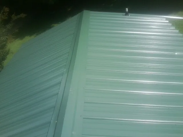 New green metal panels meeting at the ridge of a roof — Flat Roof Repair work by our crew in Callao
