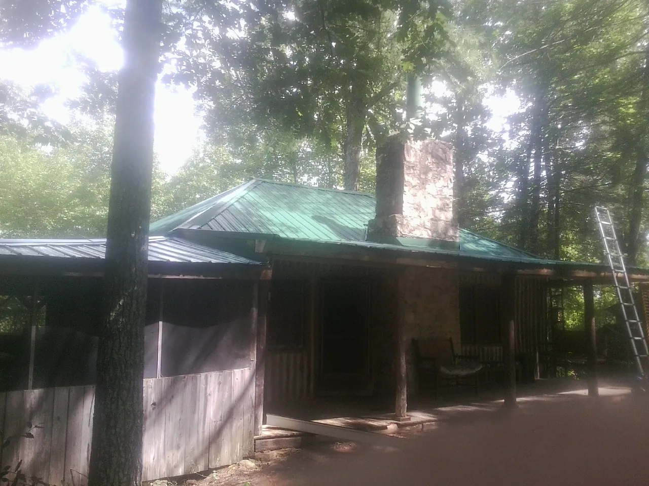 Green metal roof and stone chimney above a log cabin porch in Callao