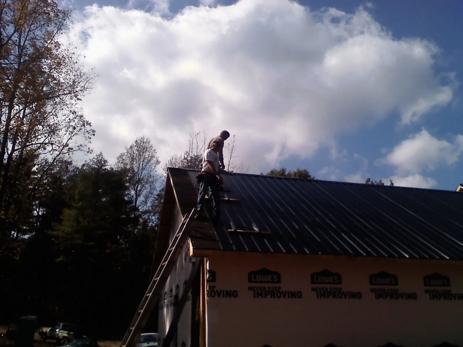 Roofer fastening dark metal panels high against a cloudy sky, from a Roof Inspection job in Callao