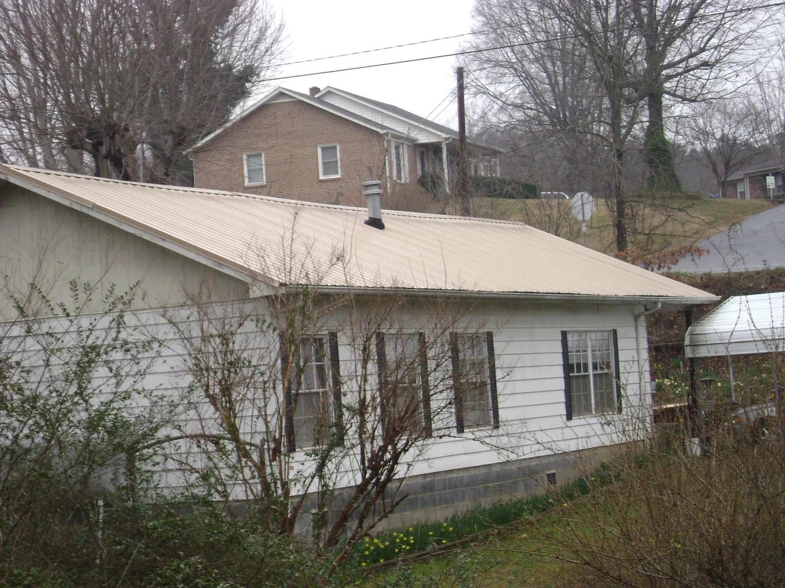 Tan metal roof on a white sided house set into a hillside — Commercial Roofing by Roofing Brothers in Callao