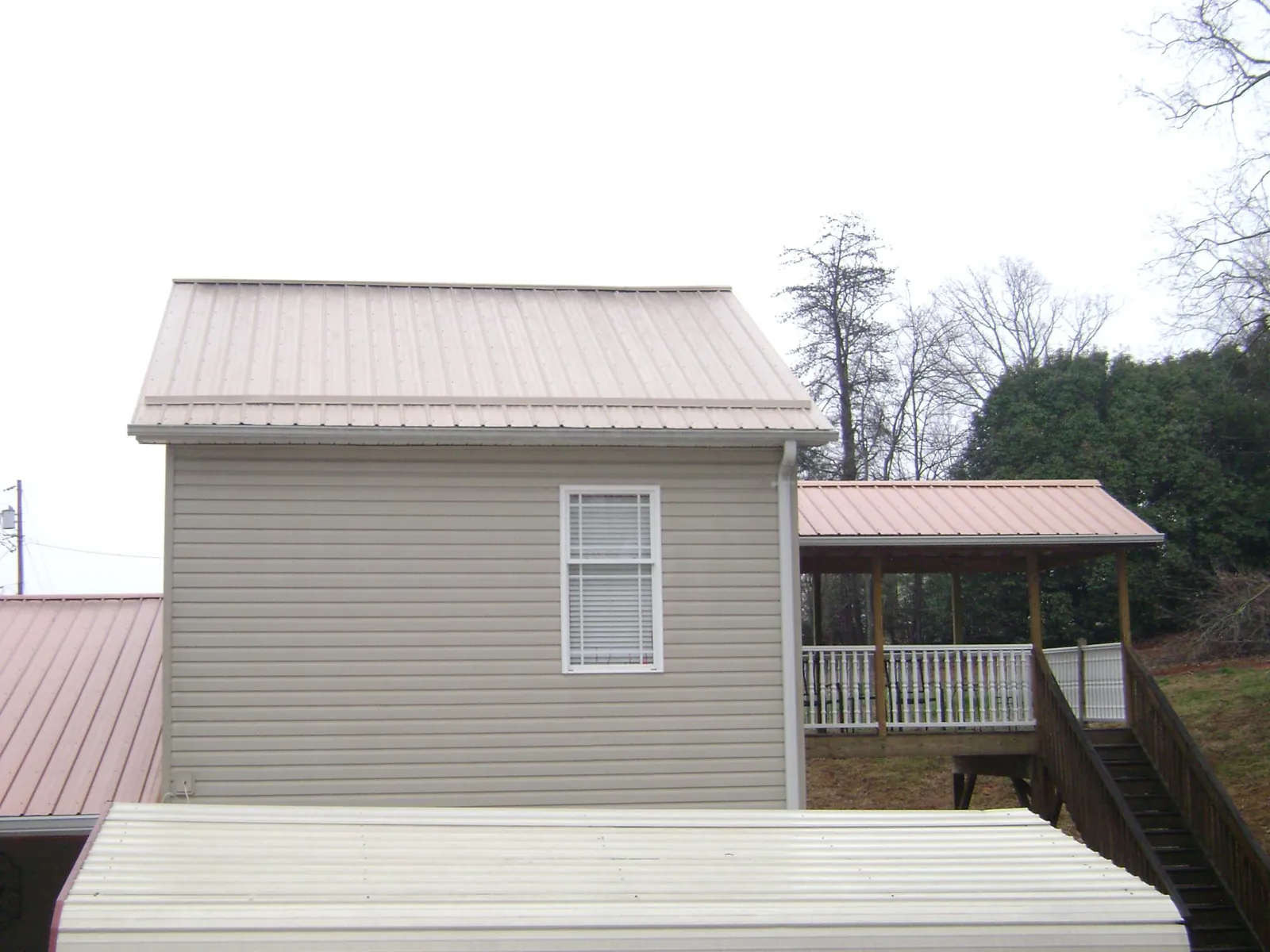 Tan metal roofs on a two story addition and attached porch, from a Roof Replacement job in Callao